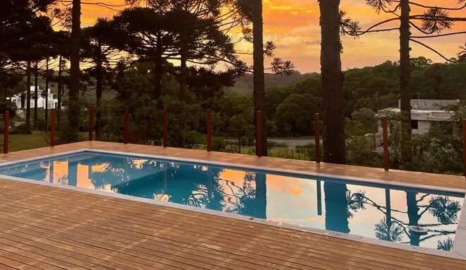 Piscina ao pôr do sol com araucárias refletidas na água, na Serra Gaúcha.