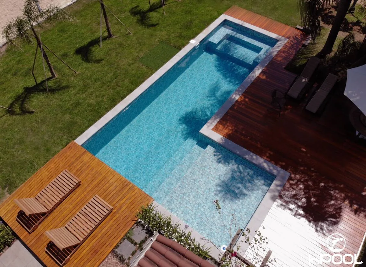 Vista aérea de piscina retangular com spa elevado, deck de madeira e espreguiçadeiras, obra da HPool.
