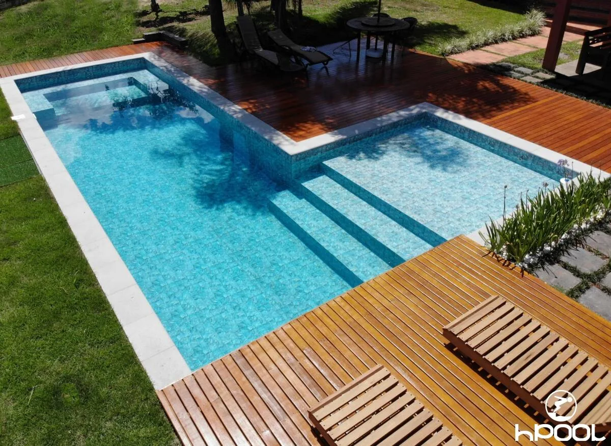 Piscina com spa elevado e degraus largos, ao lado de deck de madeira, executada pela HPool.