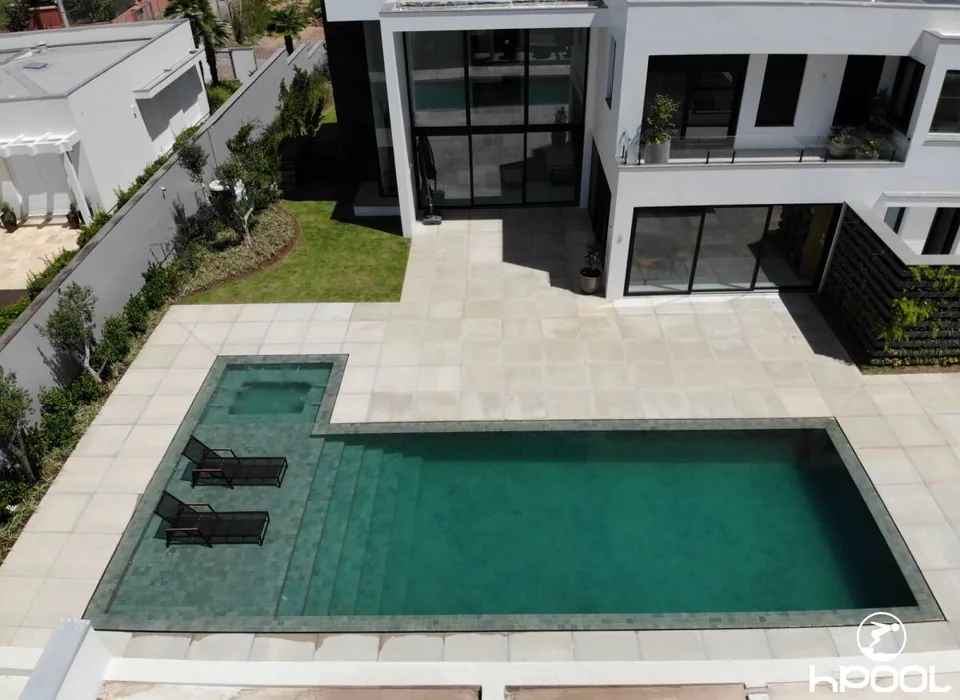 Piscina de revestimento escuro com spa integrado, junto à área social da casa.